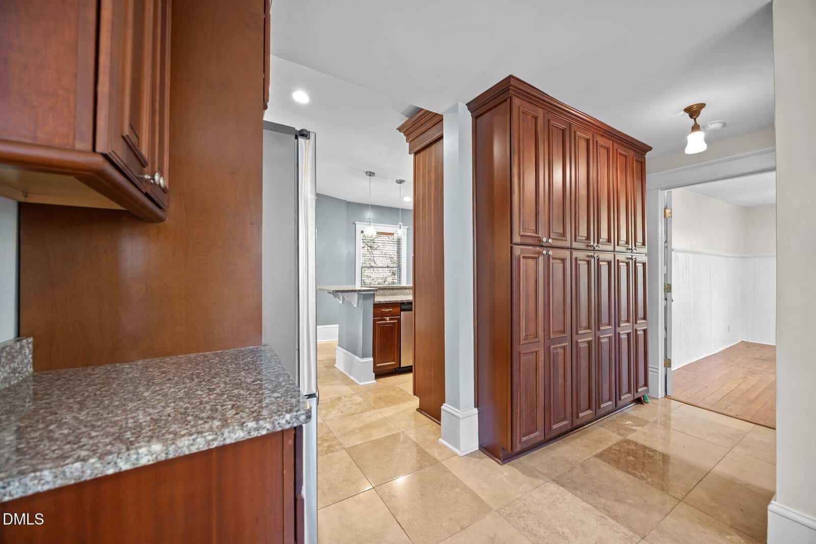 Spacious kitchen with tan tiled floor, large wooden cabinets, granite countertops, and a small breakfast bar near a window providing natural light.