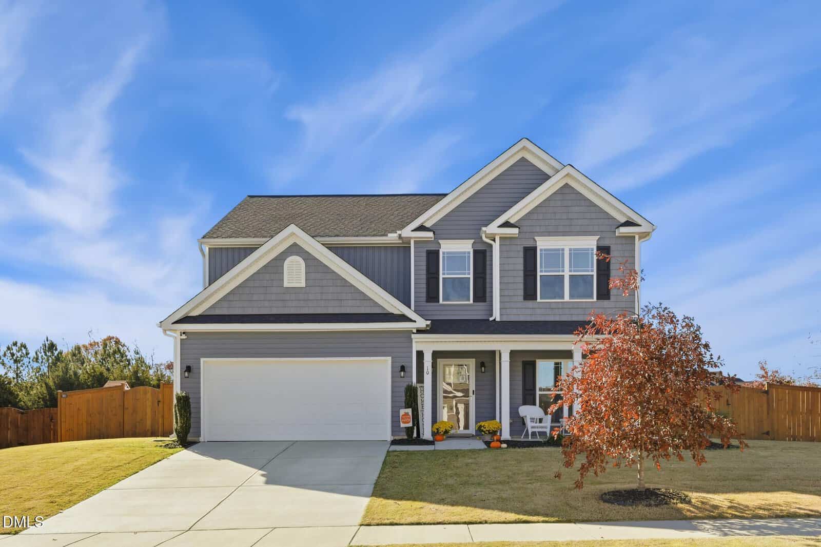 This two-story gray suburban house at 10 Cutshaw Road in Youngsville features white trim, a double garage, and a front porch. A small tree with red leaves graces the yard beneath the clear blue sky.