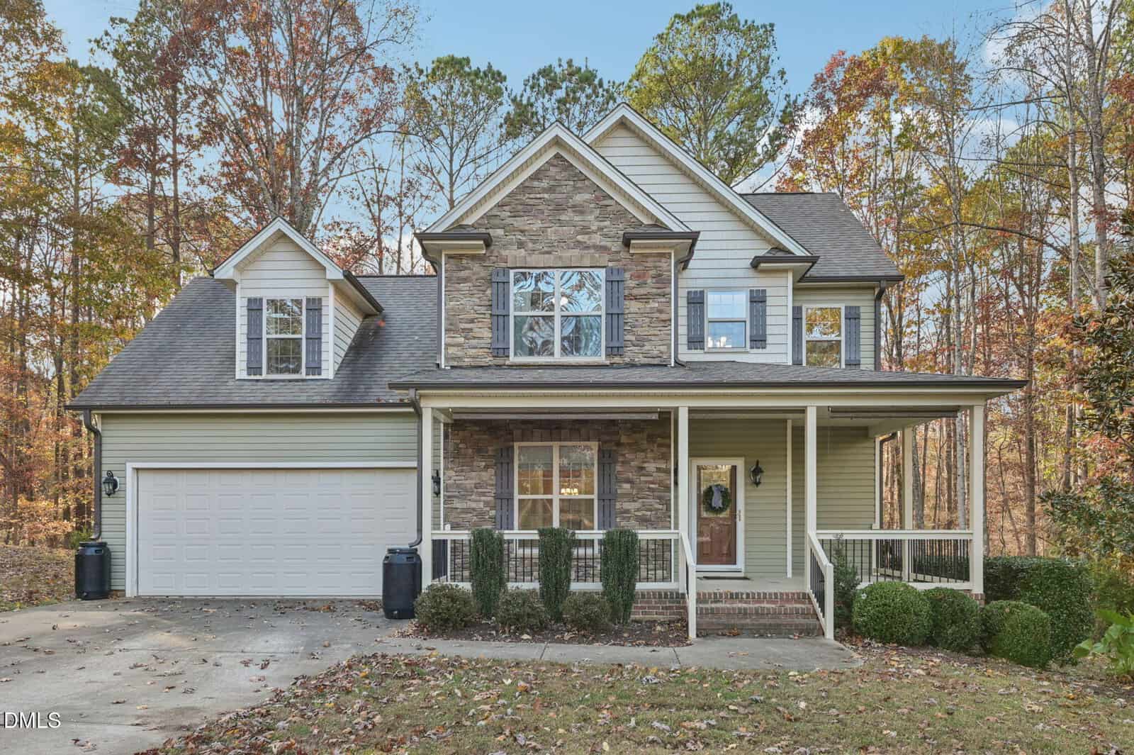 Two-story house at 35 Falcon Crest Lane, Youngsville, featuring a stone and siding exterior, attached two-car garage, covered front porch with white railings, manicured bushes, and autumn trees with fallen leaves surrounding the property.