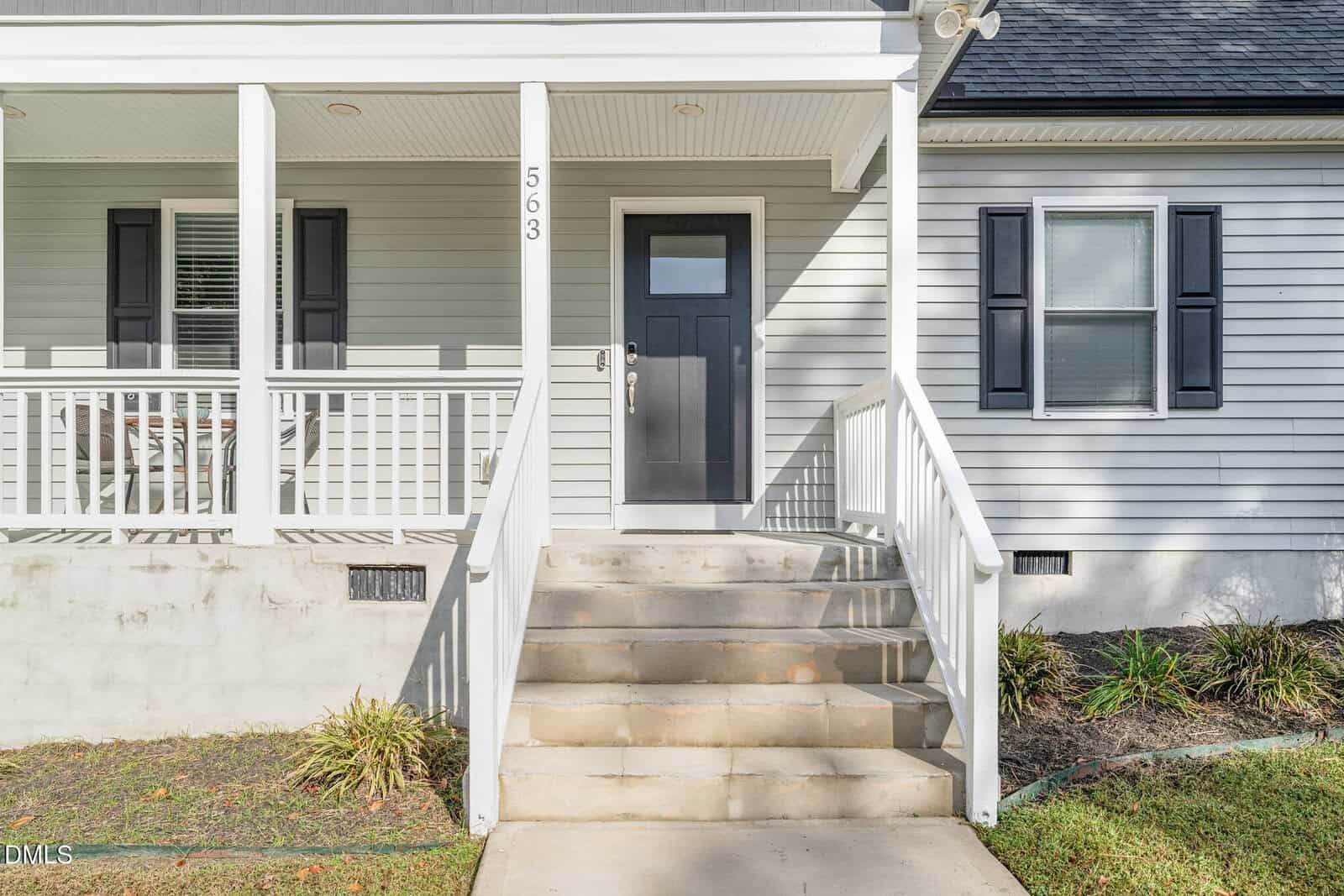 Front steps leading to a black door on a light gray house with white trim, a front porch, white railings, and a window with black shutters. House number 563 is displayed by the door.
