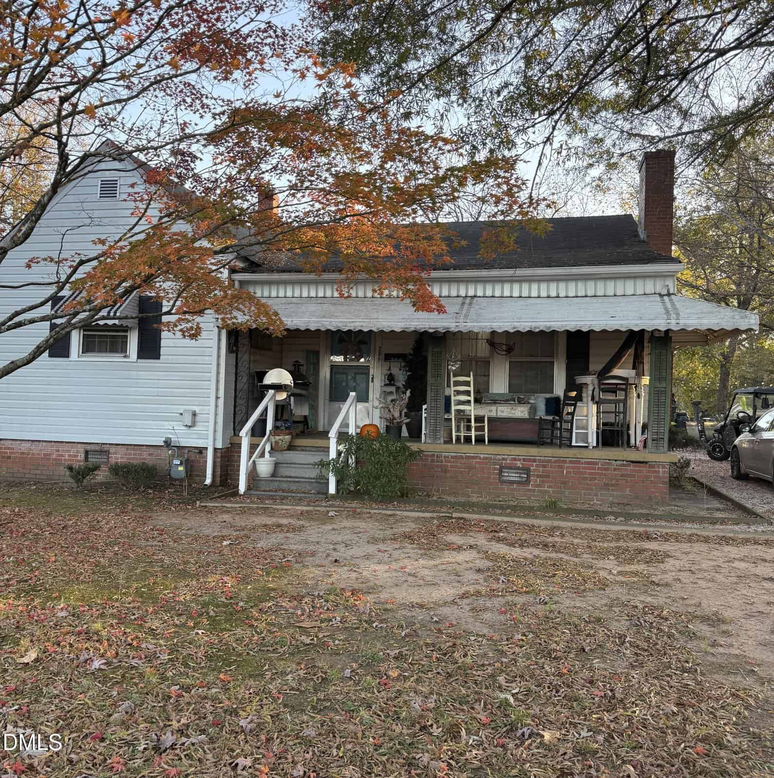 A charming one-story house at 206 Layton Street in Franklinton features light blue siding, a welcoming front porch with chairs and decorations, a sturdy brick foundation, and a sloped roof. A tree with vibrant orange leaves stands in the yard, while autumn leaves gracefully cover the ground.