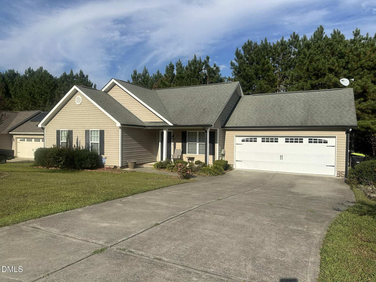 Charming single-story beige house with white trim at 109 Kinloss Way. Enjoy an attached two-car garage, concrete driveway, and a front yard filled with grass, shrubs, and a small flower bed bordered by tall pine trees that stem in the background.