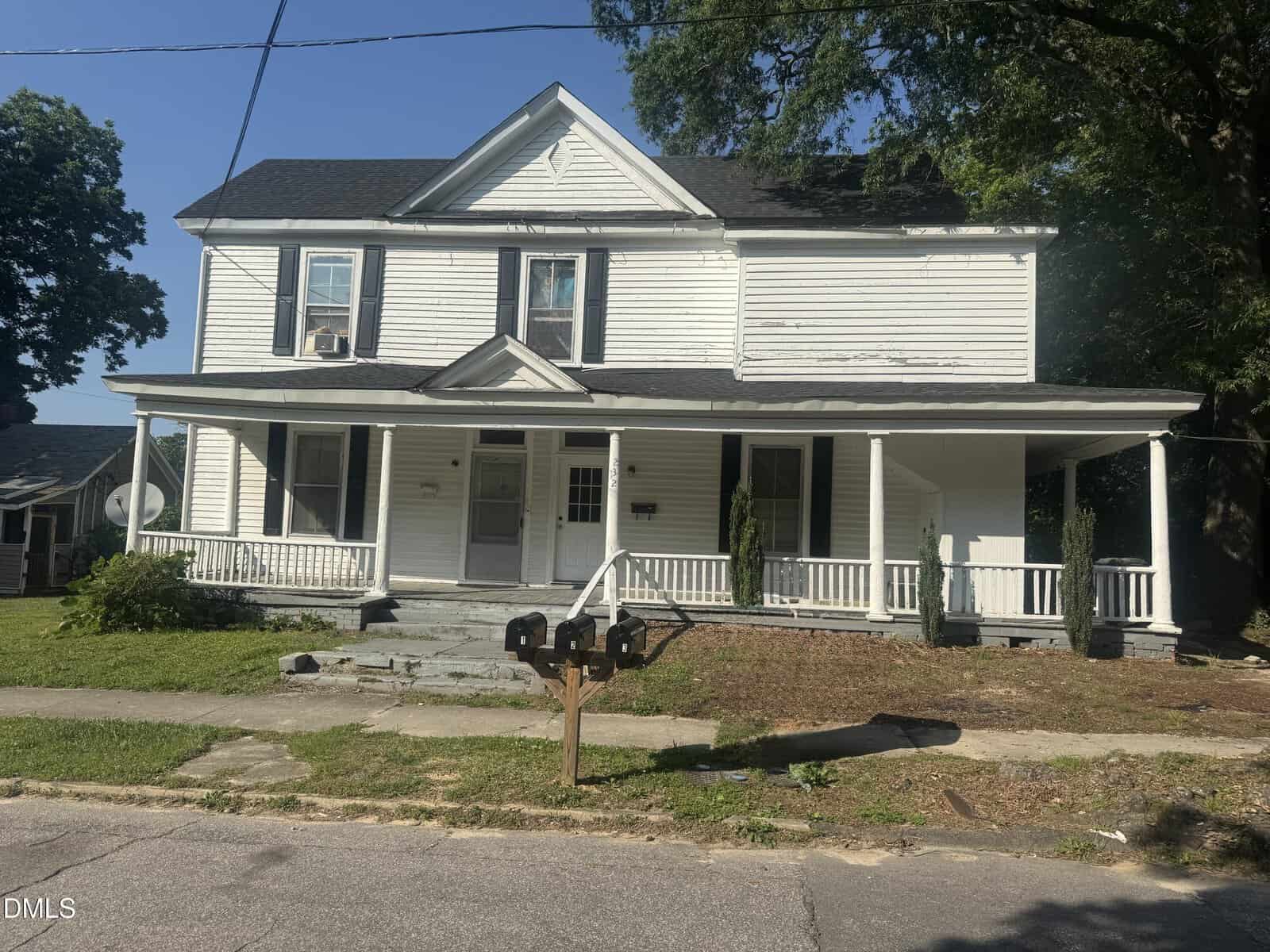 A two-story white house at 232 Burwell Avenue in Henderson features a covered front porch, two front doors, three black mailboxes by the street, with trees and grass in the yard. The siding and steps show signs of wear.