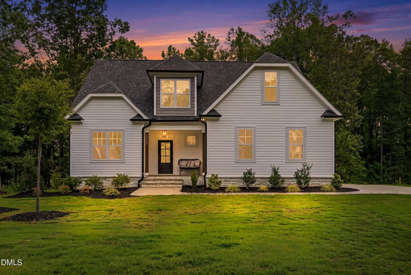 A modern two-story gray house with white trim, front porch, and well-kept landscaping, set against a backdrop of trees at sunset, located at 12874 Mallard Rock Drive in charming Zebulon.