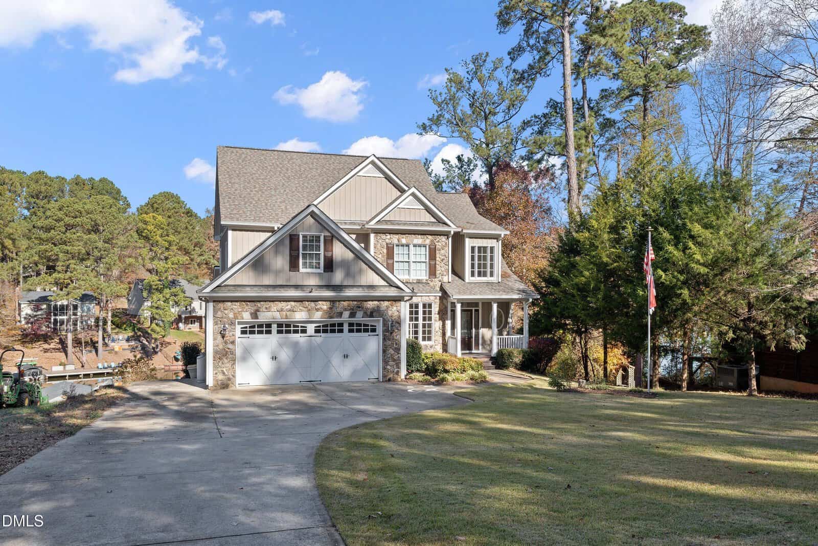 A two-story suburban house at 737 Sagamore Drive, Louisburg, with stone and siding exterior, a double garage, and large windows. It sits on a spacious lot with a curved driveway, lawn, and trees under a clear blue sky.