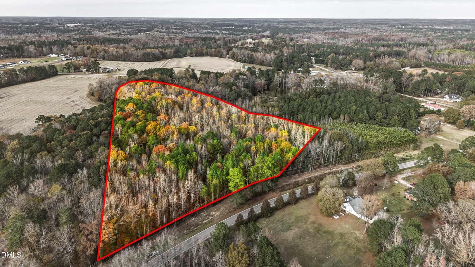 Aerial view of a wooded plot of land at 0 Old US Highway 64, Spring Hope, outlined in red, containing trees with various shades of green, yellow, and orange, bordered by a road and surrounded by fields and rural properties.