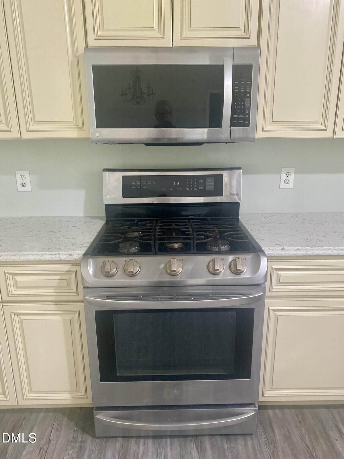 Stainless steel gas range with oven and matching microwave above, set against light-colored cabinets and a granite countertop in a kitchen.