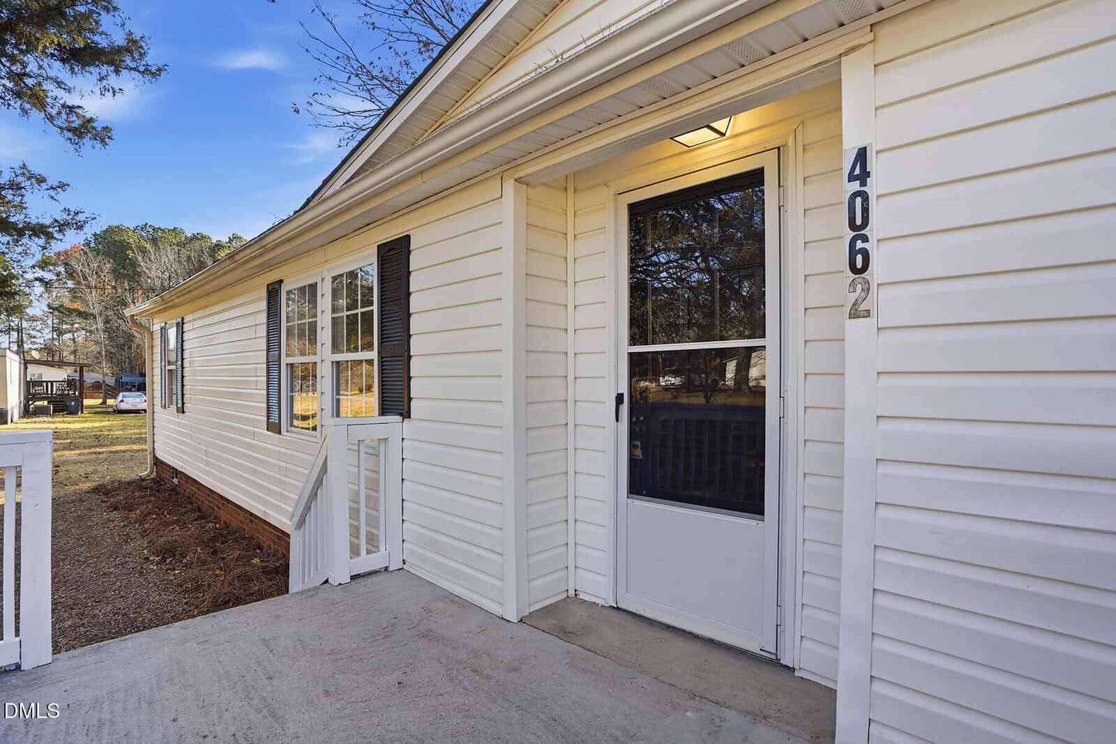 Single-story white house with horizontal siding, a glass storm door, and house number 4062 beside the entrance. A walkway leads to the front porch. Windows with black shutters are on the side of the house.