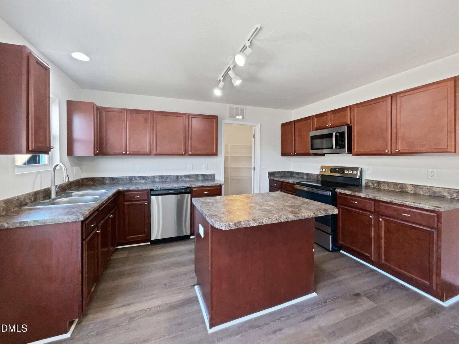 Spacious kitchen with dark wood cabinets, brown granite countertops, stainless steel appliances, a central island, and dark wood flooring under bright ceiling lights.
