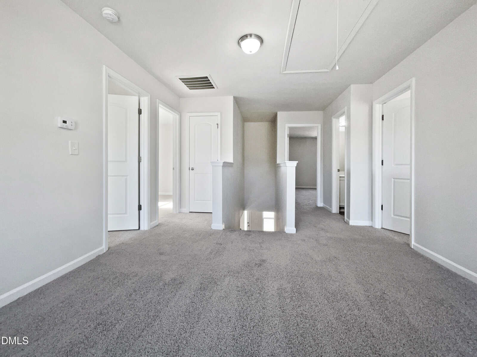 A bright hallway with gray carpet, white walls, four closed white doors, and a small staircase opening in the center, lit by a ceiling light.