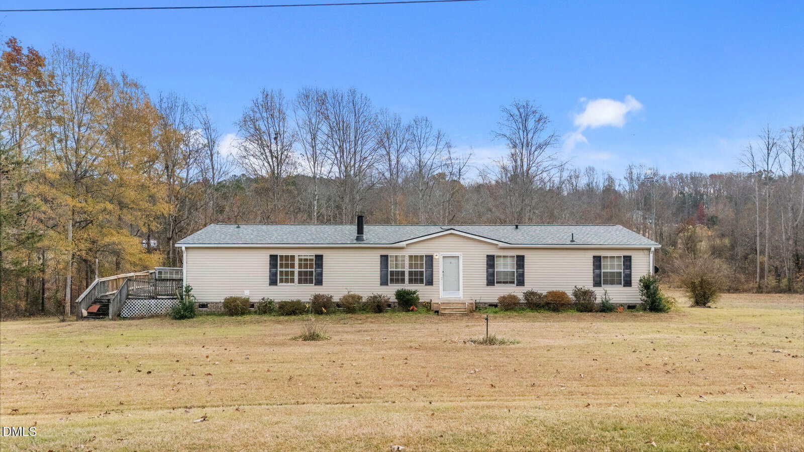 A single-story manufactured home with light-colored siding, dark shutters, and a gray shingle roof sits on a large grassy lot at 2562 Moss Ledford Road in Franklinton, with sparse bushes in front and leafless trees in the background.