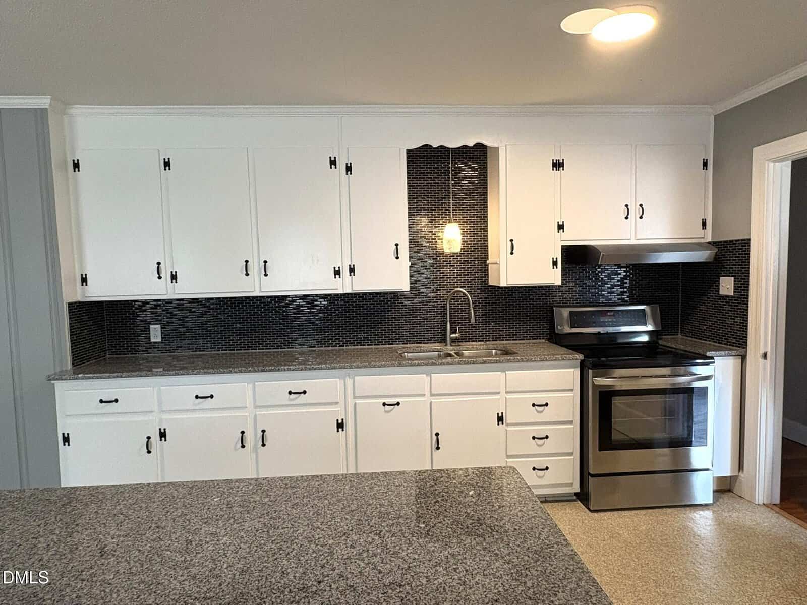 Modern kitchen with white cabinets, stainless steel appliances, a granite countertop, and a dark tile backsplash. There’s a sink under a wall light and an electric stove with a range hood on the right side.