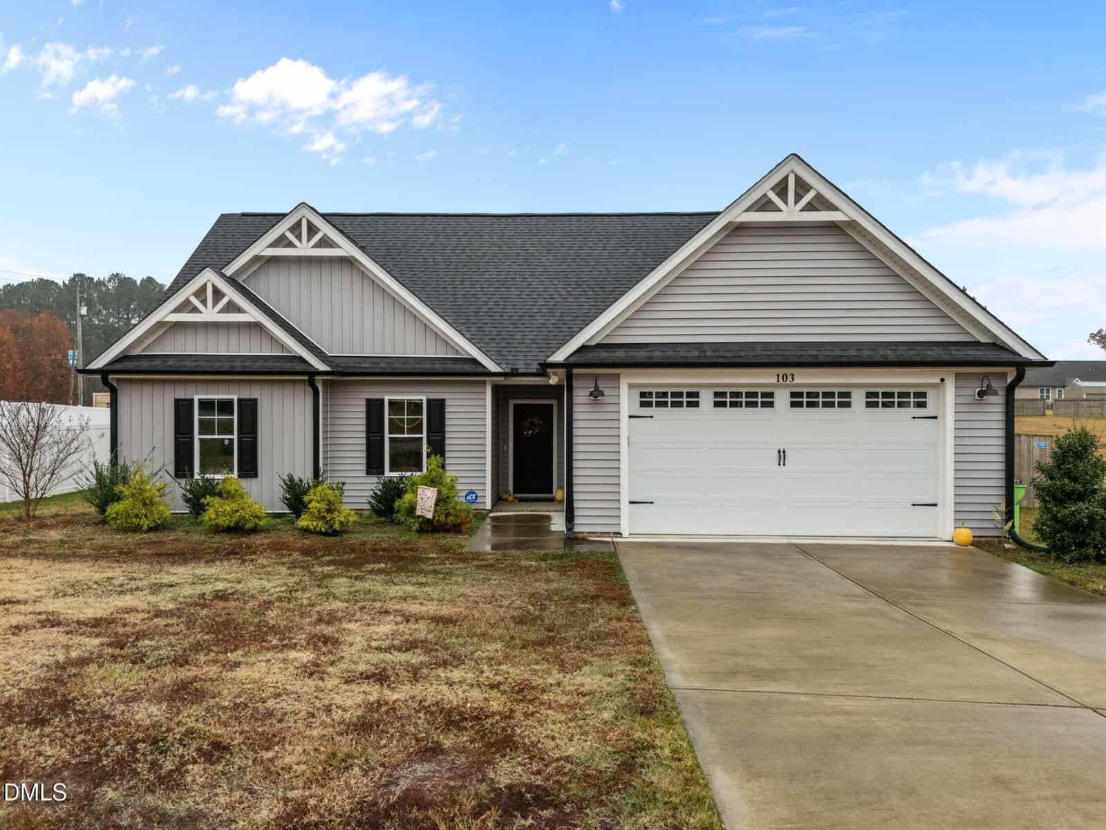 A single-story gray house with white trim and a black roof at 103 Averly Court, Stem. This home features a two-car garage, manicured shrubs, patchy front lawn, concrete driveway, and a walkway leading to the entry door.