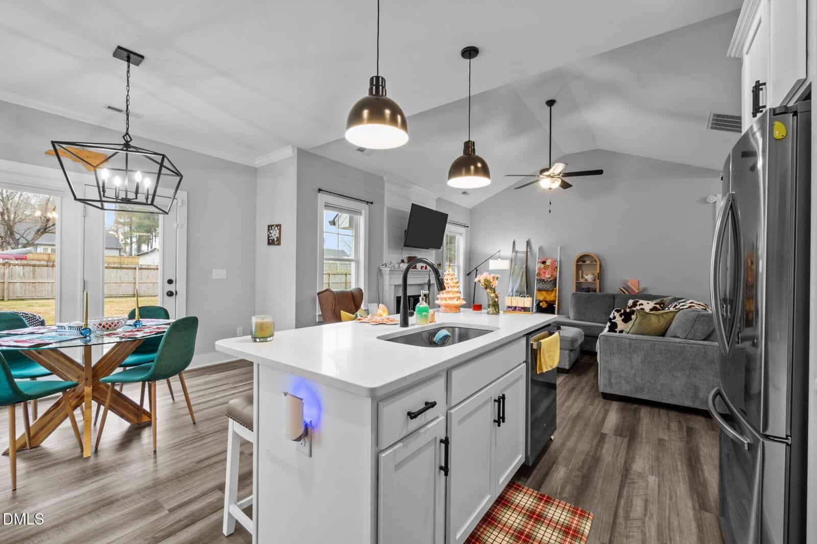 Modern open-concept kitchen and living room with white cabinets, island, dining table, gray sofa, and holiday decorations. Large windows and pendant lights provide bright, cozy atmosphere.