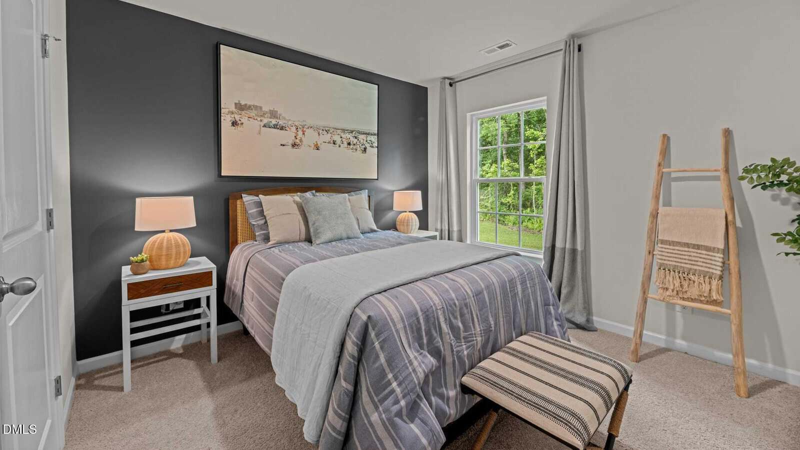A neatly made bed with striped bedding is centered in a bedroom with gray accent wall. Two nightstands with lamps flank the bed. A window with gray curtains lets in natural light. A ladder shelf and a bench are beside the bed.
