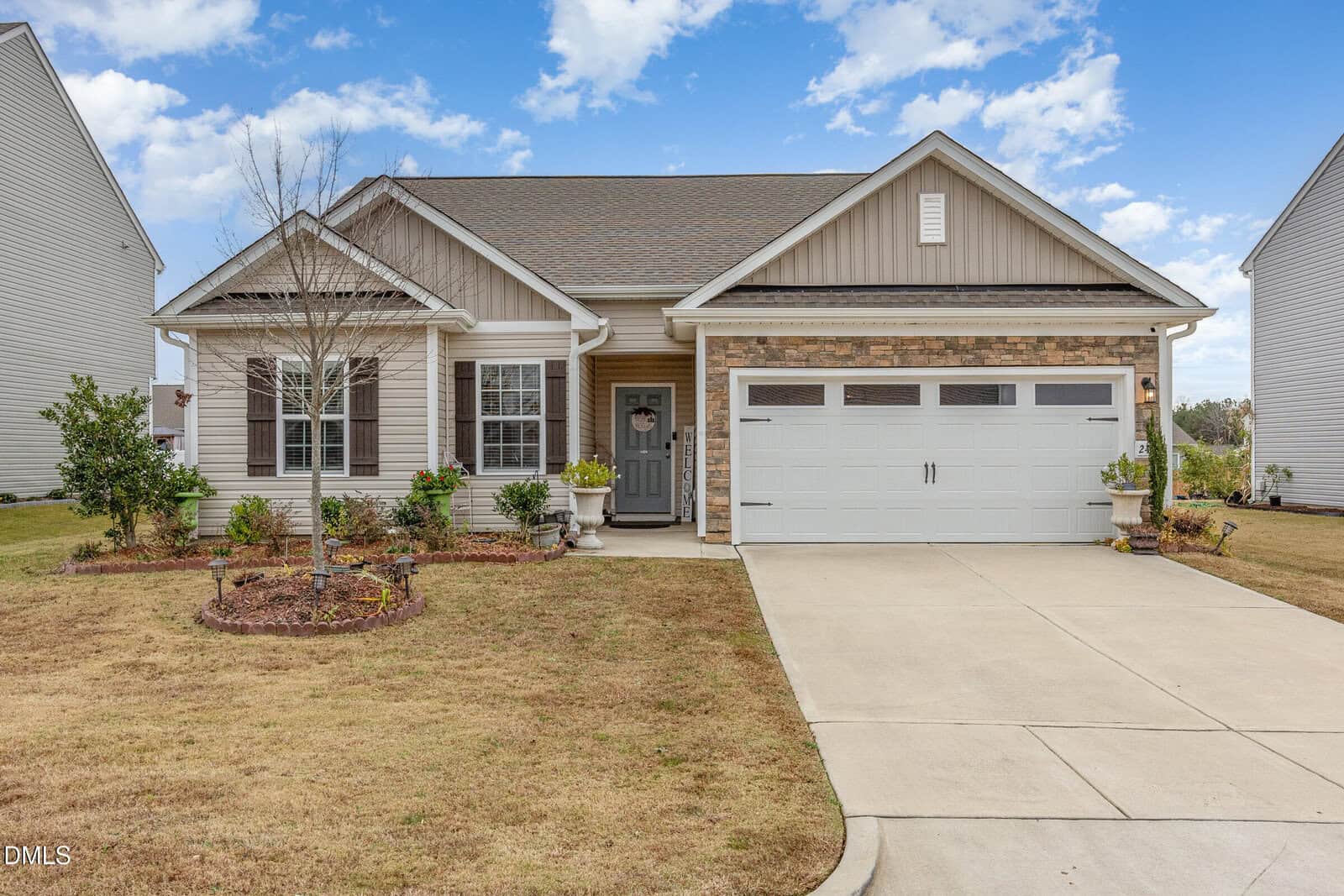 Single-story suburban house with beige siding, stone accents, a gray front door, white trim, and a two-car garage located at 245 Access Drive in Youngsville. The yard features trimmed grass, small shrubs, a young tree, and a paved driveway under a partly cloudy sky.
