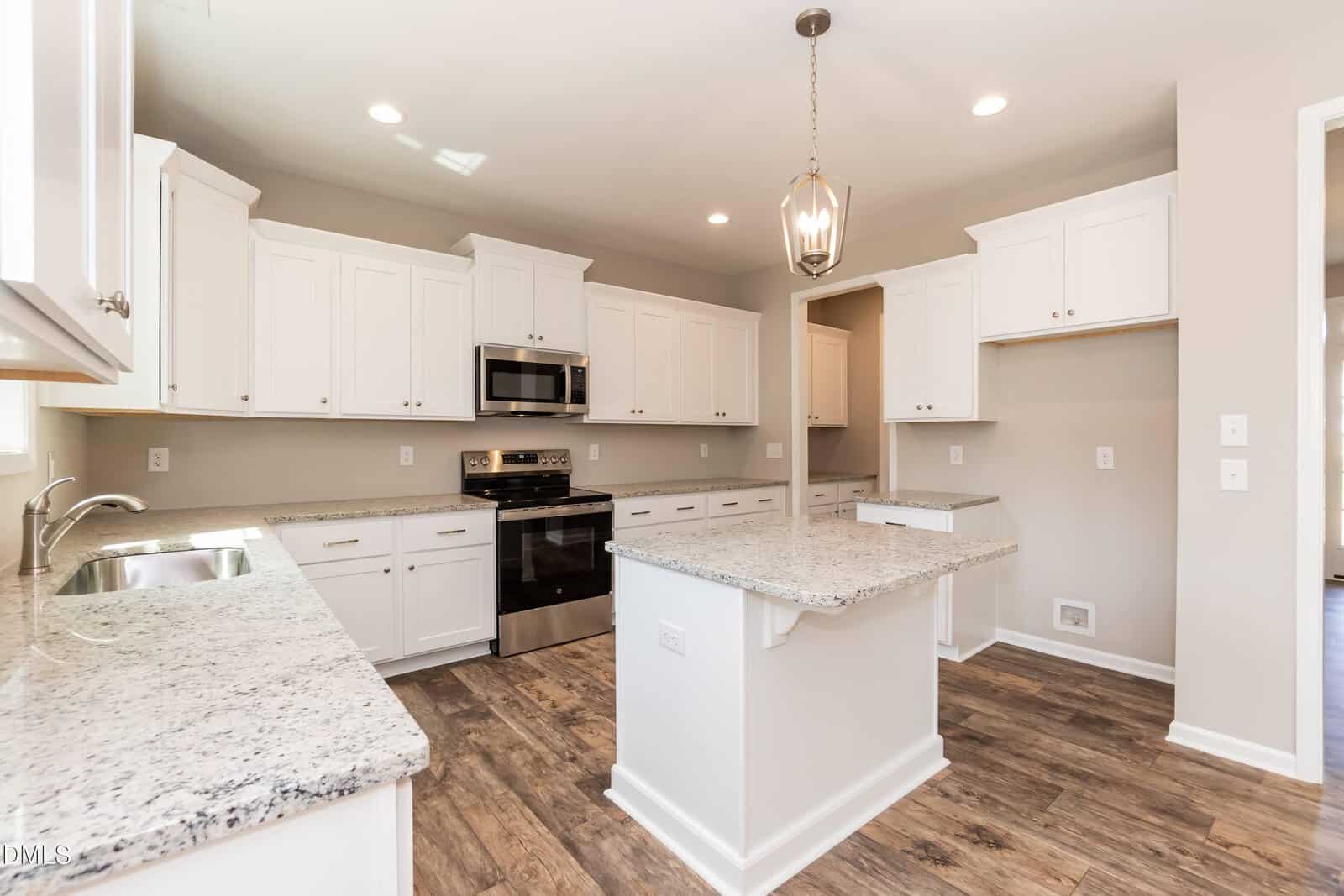Modern kitchen with white cabinets, granite countertops, stainless steel appliances, a central island with a pendant light above, and wood-style flooring. The space is bright with neutral walls and recessed lighting.