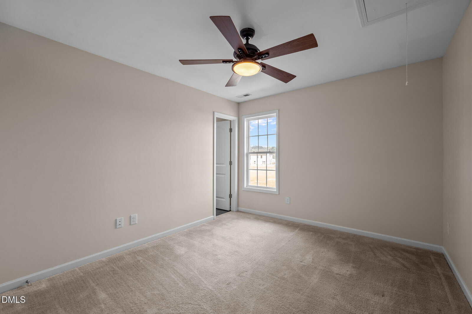 Empty beige bedroom with carpeted floor, ceiling fan, single window, and a door leading to another room or closet.