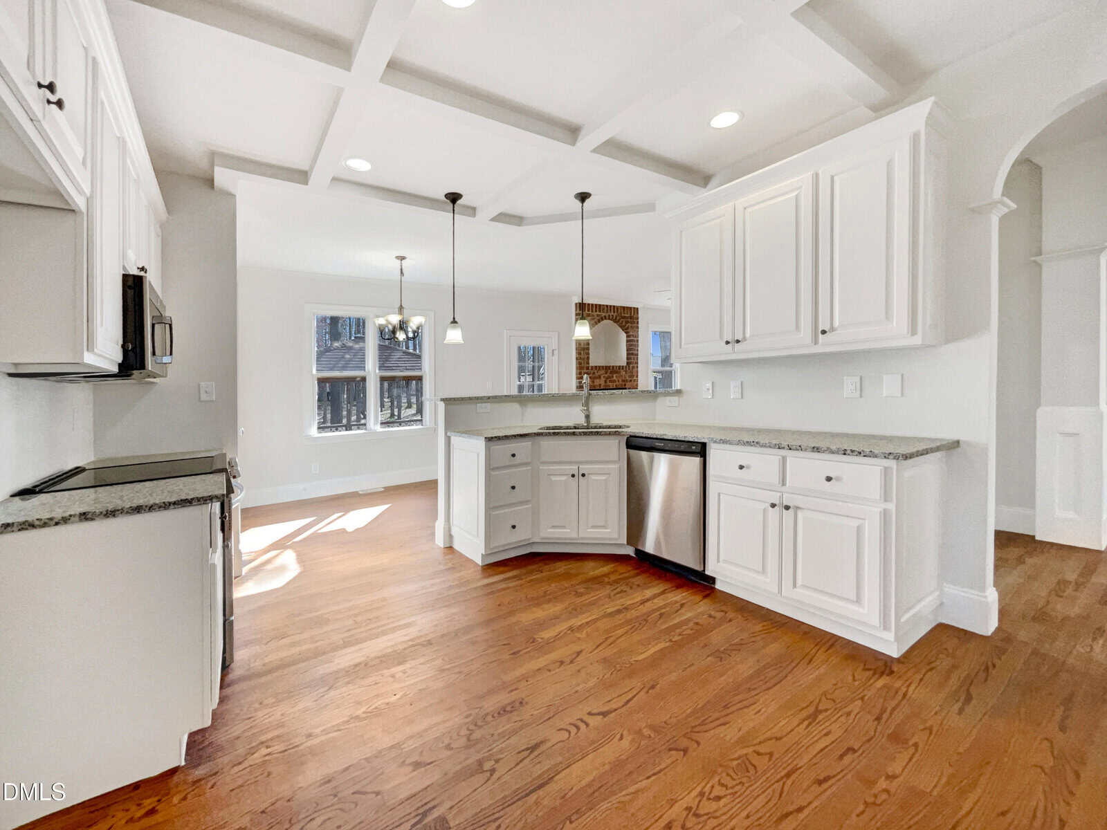 Bright, modern kitchen with white cabinets, stainless steel appliances, granite countertops, pendant lights, hardwood floors, and large windows letting in natural light.