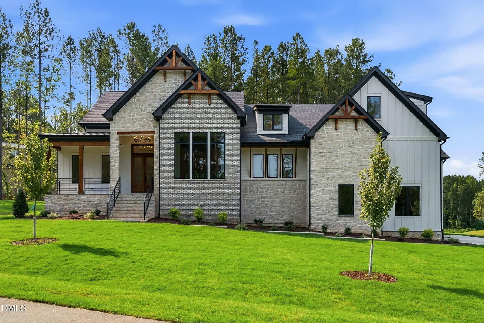 Modern house at 85 Ashbrooke Falls Drive, Franklinton, featuring light brick and white siding, black trim, a front porch, multiple large windows, and a neatly landscaped front yard with green grass and young trees—all set against a backdrop of tall pine trees.