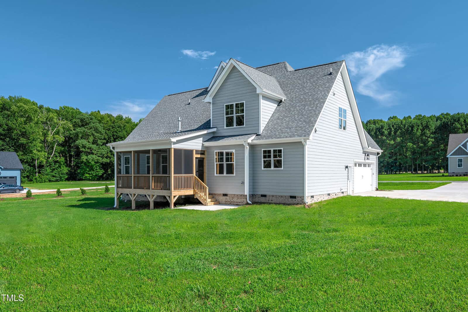 A two-story white house with gray roofing sits on a large, neatly mowed green lawn. The home features a screened porch, multiple windows, and an attached two-car garage. Trees line the background.