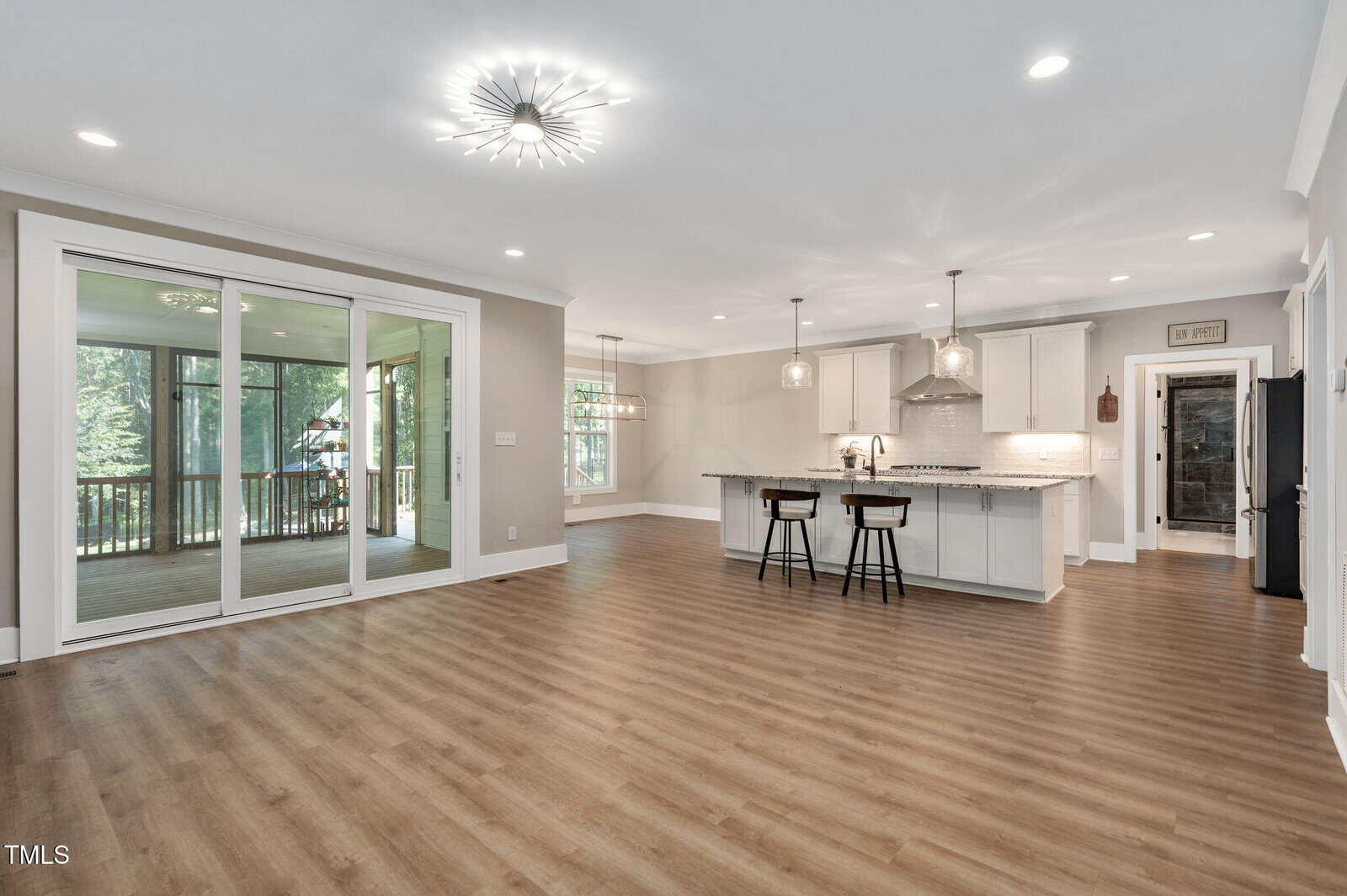 Open-concept kitchen and living area with wood floors, white cabinetry, pendant lights over an island, sliding glass doors to a screened porch, and a modern chandelier on the ceiling.
