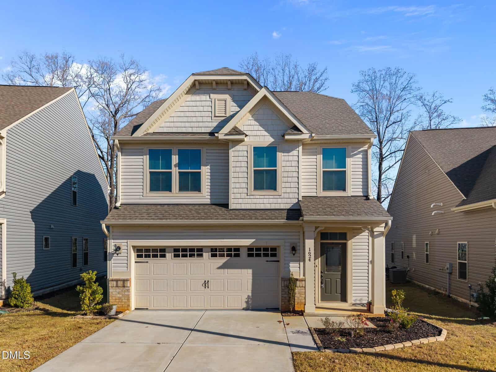 A two-story, beige suburban house with a double garage, front porch, and small landscaped yard at 1624 Ripley Woods Street in Wake Forest, nestled between similar homes on a sunny day.