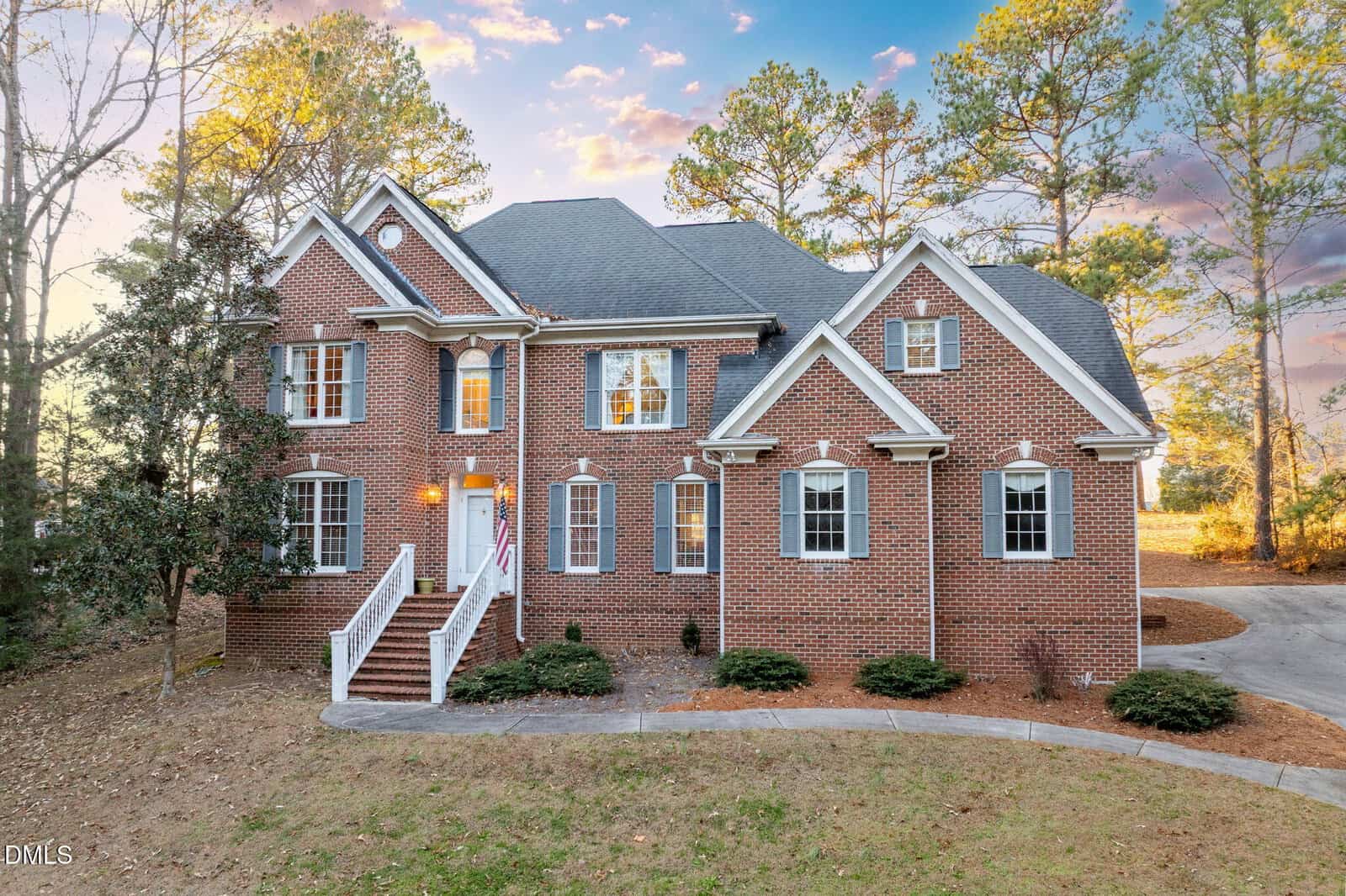 This two-story brick house at 1806 Waddill Way in Henderson features multiple gables, white trim, and a front staircase. Surrounded by trees, the property includes a curved driveway on the right side.