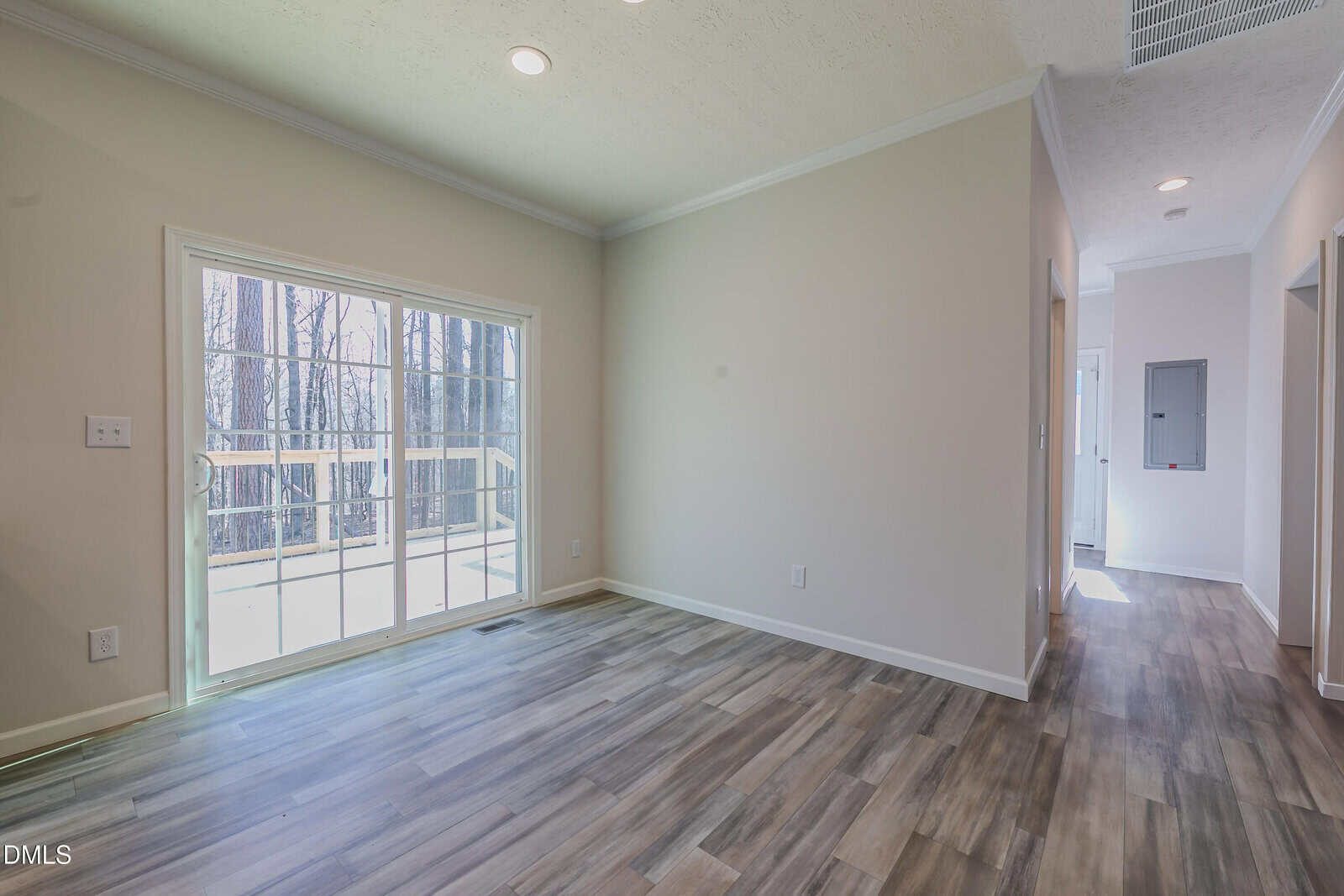 An empty room with a sliding glass door leading to a deck. Wood-style flooring and neutral walls. A hallway is visible to the right.
