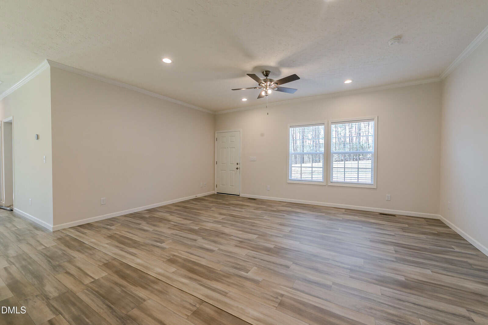 Spacious empty living room with light beige walls, wood-look tile flooring, ceiling fan with lights, recessed lighting, two large windows, and a white door. Natural light fills the room.