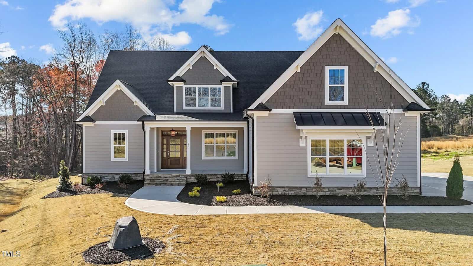 A modern two-story house with gray siding, white trim, and a dark roof, featuring multiple front-facing gables, large windows, a covered porch, and a neatly landscaped front lawn under a blue sky.