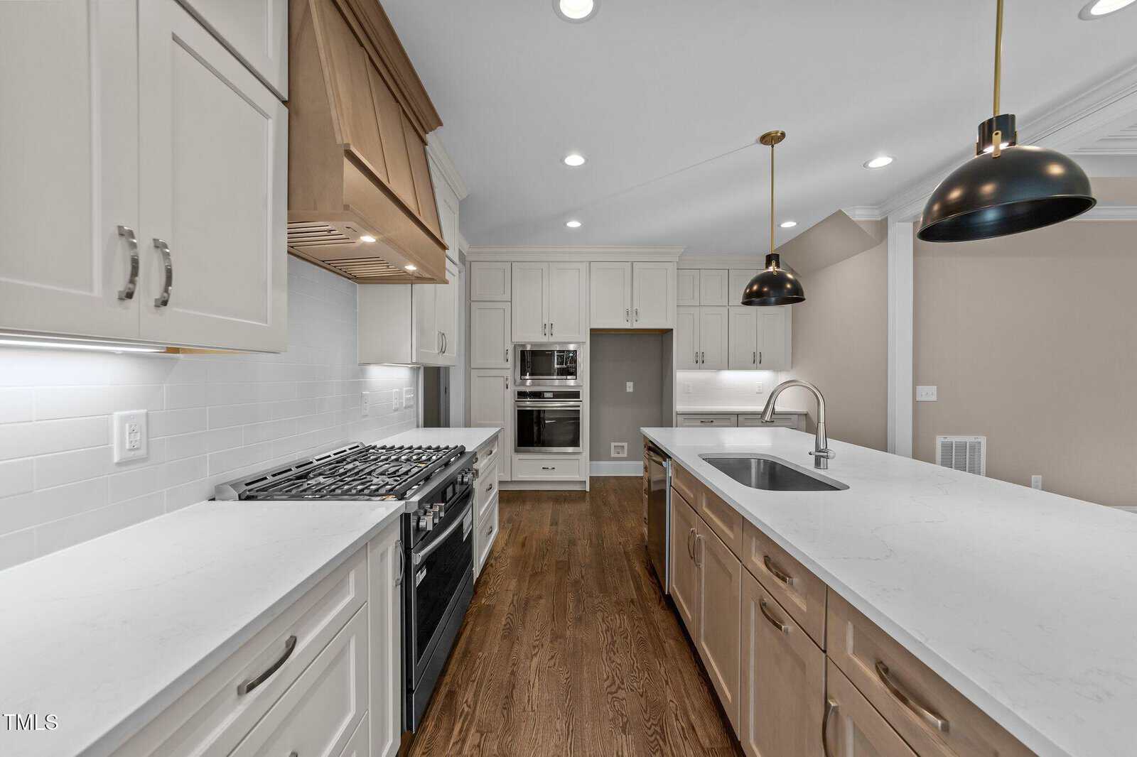 Modern kitchen with white cabinets, stainless steel appliances, a gas stove, built-in oven, white subway tile backsplash, center island with sink, pendant lights, and medium tone wood flooring.