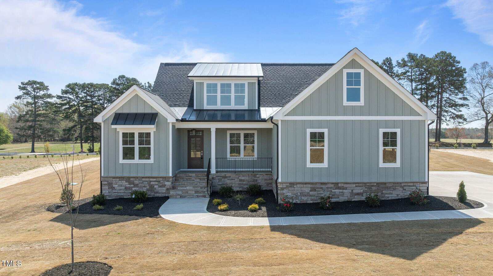 This modern two-story house at 35 Wheatfield Lane in Youngsville features light gray siding, white trim, a stone foundation, multiple gabled roofs, a front porch, and is surrounded by a circular driveway and sparse landscaping.