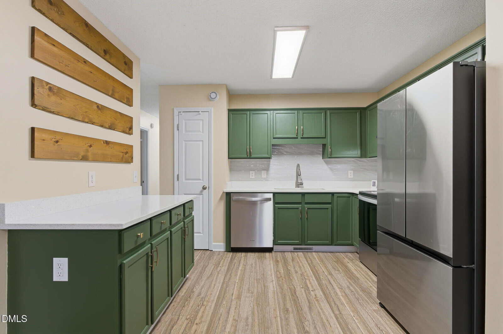 Modern kitchen with green cabinets, white countertops, stainless steel appliances, wood flooring, and wooden wall accents, featuring a bright, clean, and contemporary design.