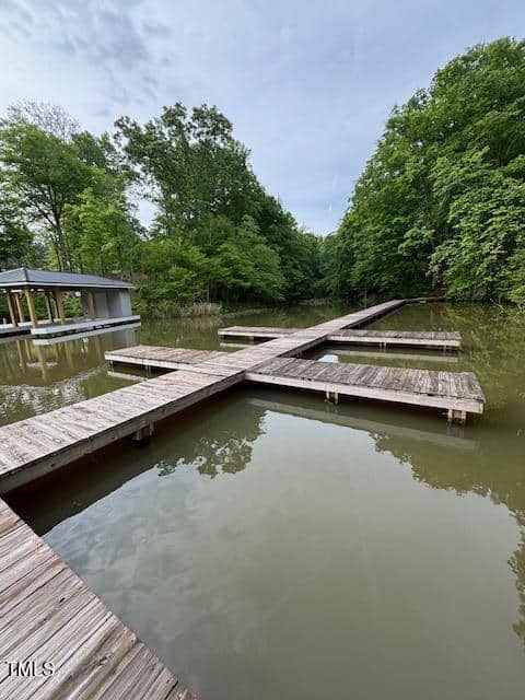 Wooden docks form a T-shape over calm, reflective water, surrounded by dense green trees at 5 Pinnacle Shores Drive, Macon. A covered dock structure is visible to the left. The sky is overcast.