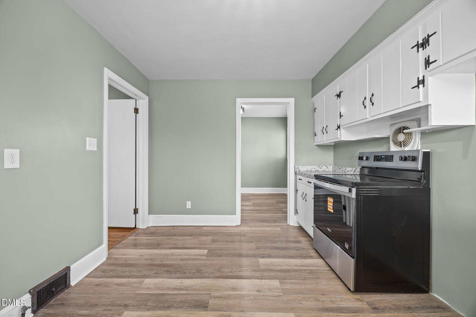 A kitchen with light green walls, white cabinets, granite countertops, a black stove, and wood-look flooring. Two doorways lead to adjacent rooms, one of which has hardwood floors.