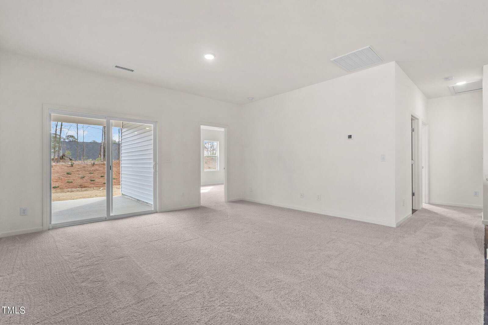 Spacious, unfurnished room with light carpet, white walls, sliding glass doors to a patio, and doorways leading to other rooms. Natural light enters from the patio doors.