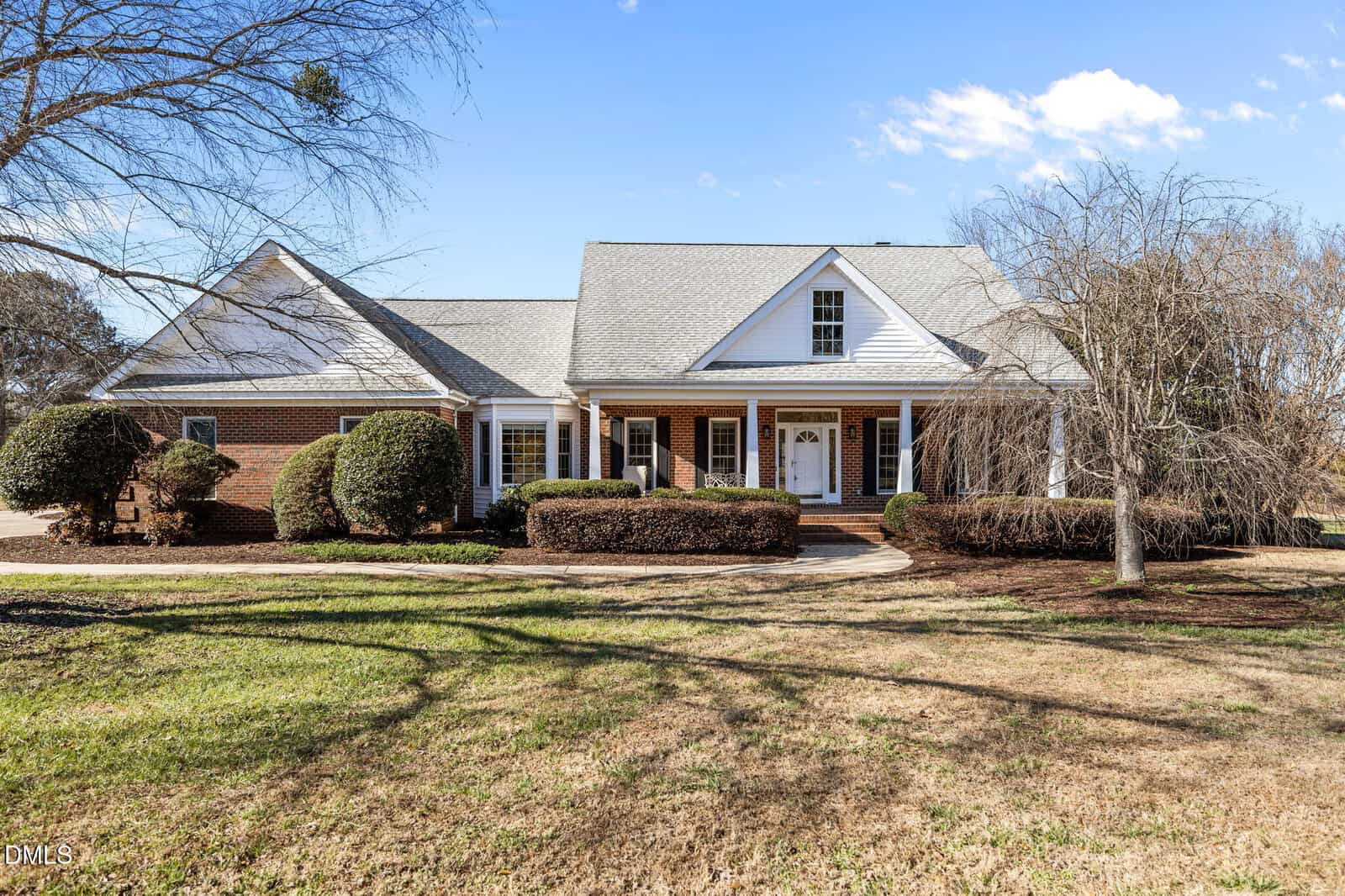 Single-story brick and siding house with a covered front porch, dormer window, white columns, manicured bushes, and a lawn with bare trees under a clear blue sky—all nestled on 102 Derby Lane in the heart of Franklinton.