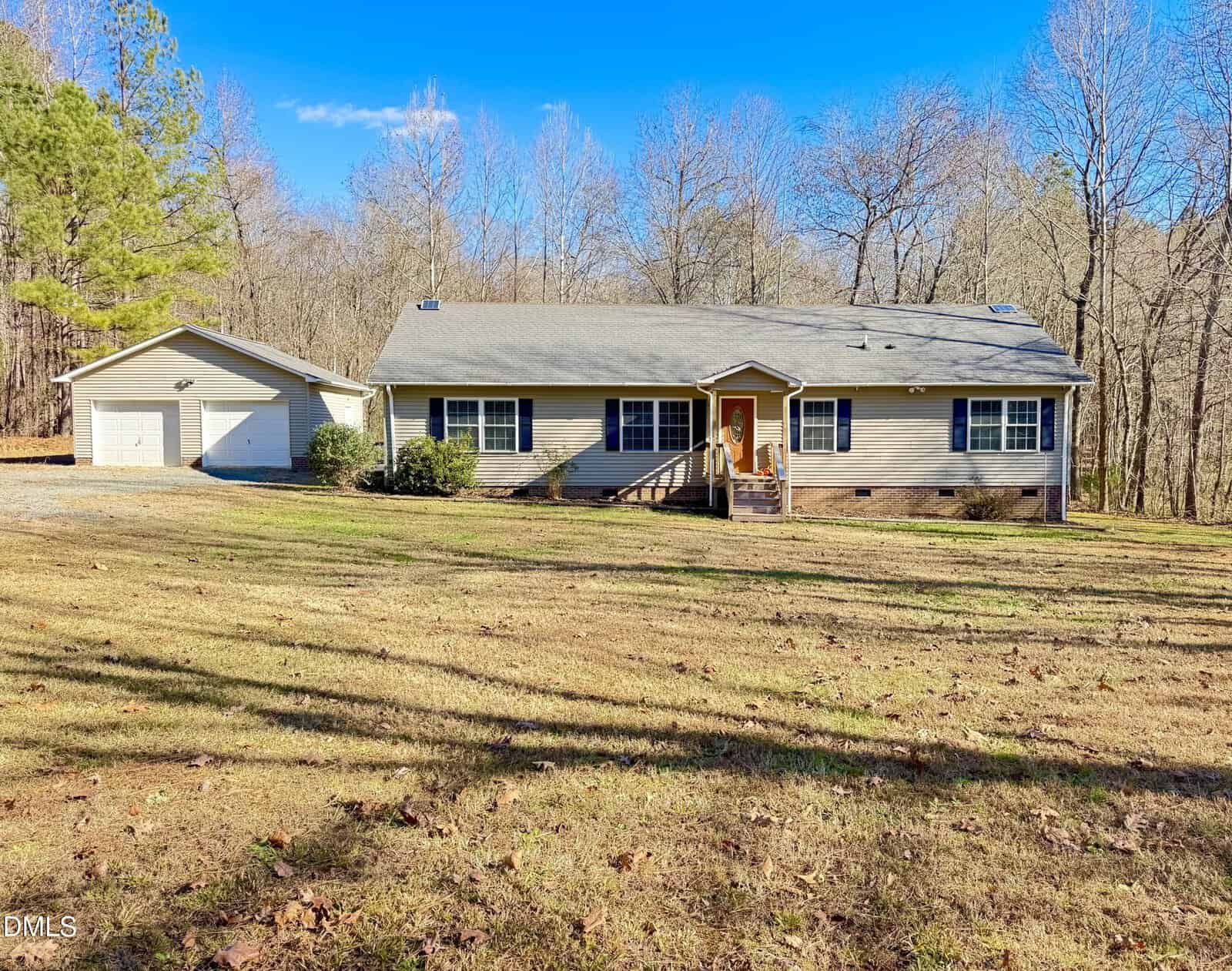 Charming single-story beige house with a gray roof and front porch at 4632 Culbreth Road, Oxford. Set on a spacious lawn scattered with leaves, it features a detached two-car garage and is surrounded by leafless trees under a clear blue sky.