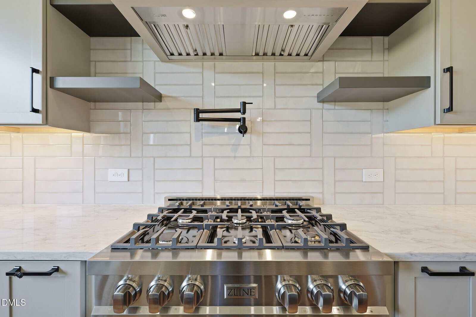 Modern kitchen with a stainless steel gas stove, marble countertop, light tile backsplash, a pot filler faucet above the stove, and two floating shelves on each side.