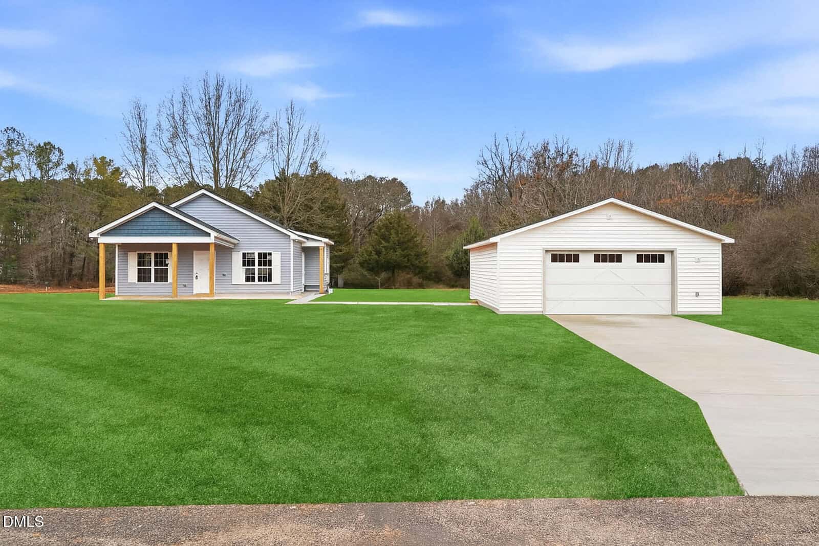 A small gray house with a covered porch sits on a large green lawn at 11 Halifax Avenue, Louisburg, next to a detached white garage, with a long driveway and trees in the background under a blue sky.
