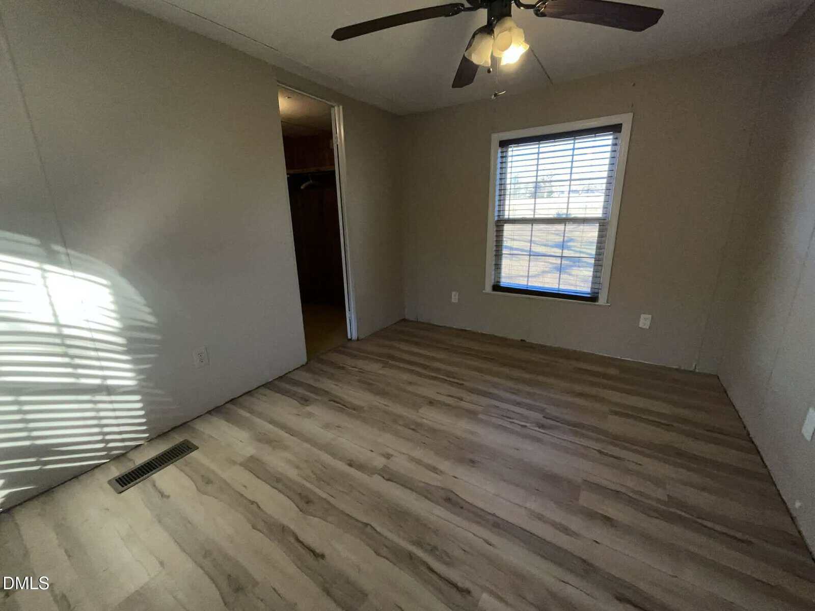 Empty room with light wood flooring, beige walls, a ceiling fan with lights, a window with blinds letting in sunlight, and an open doorway leading to a closet area.