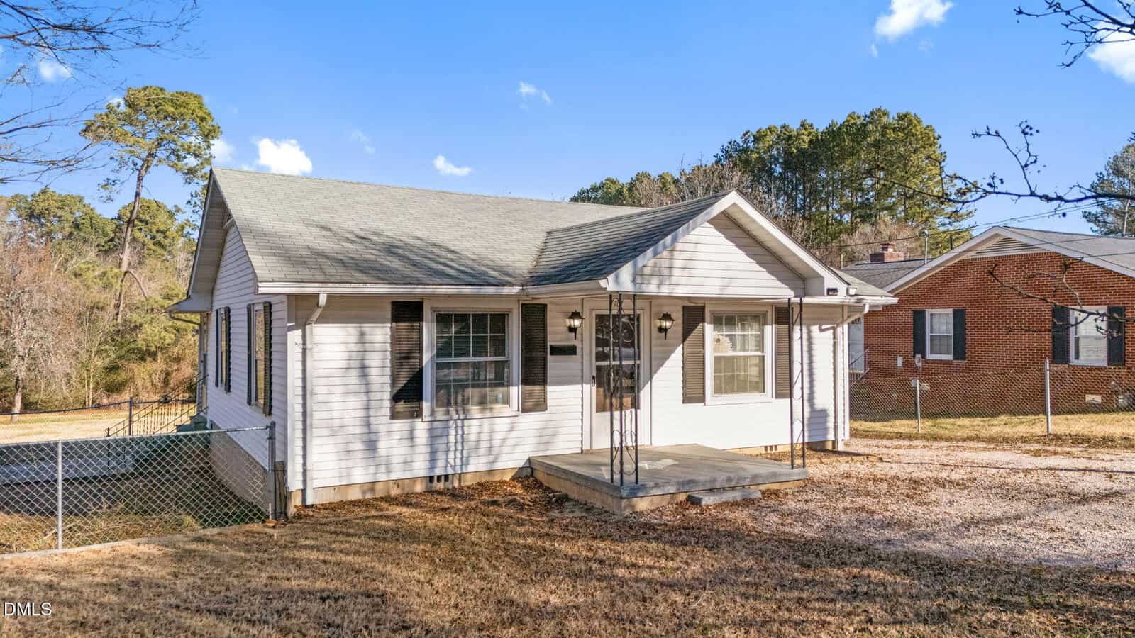 Charming single-story white house at 707 E Mason Street in Franklinton, featuring a small covered front porch, black shutters, gray roof, and a partly fenced yard. A neighboring brick home is also nearby.