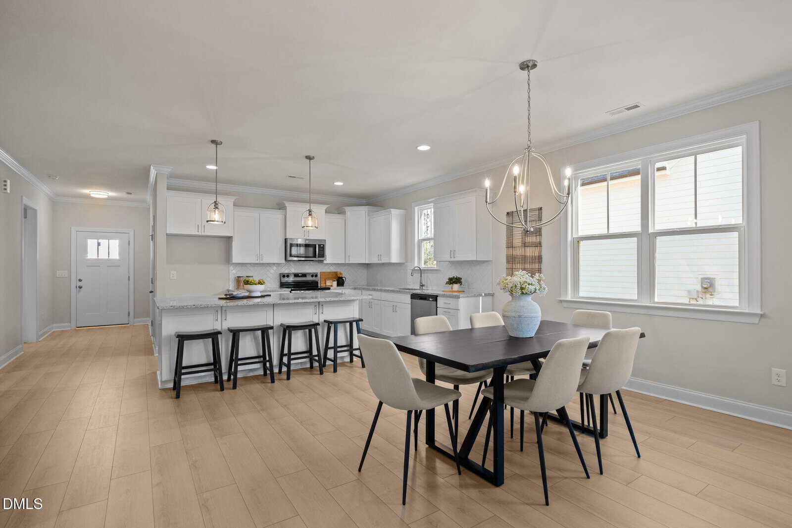 Open-concept kitchen and dining area with light wood floors, white cabinets, a large island with barstools, modern pendant lighting, and a black dining table set for six beneath a decorative chandelier.