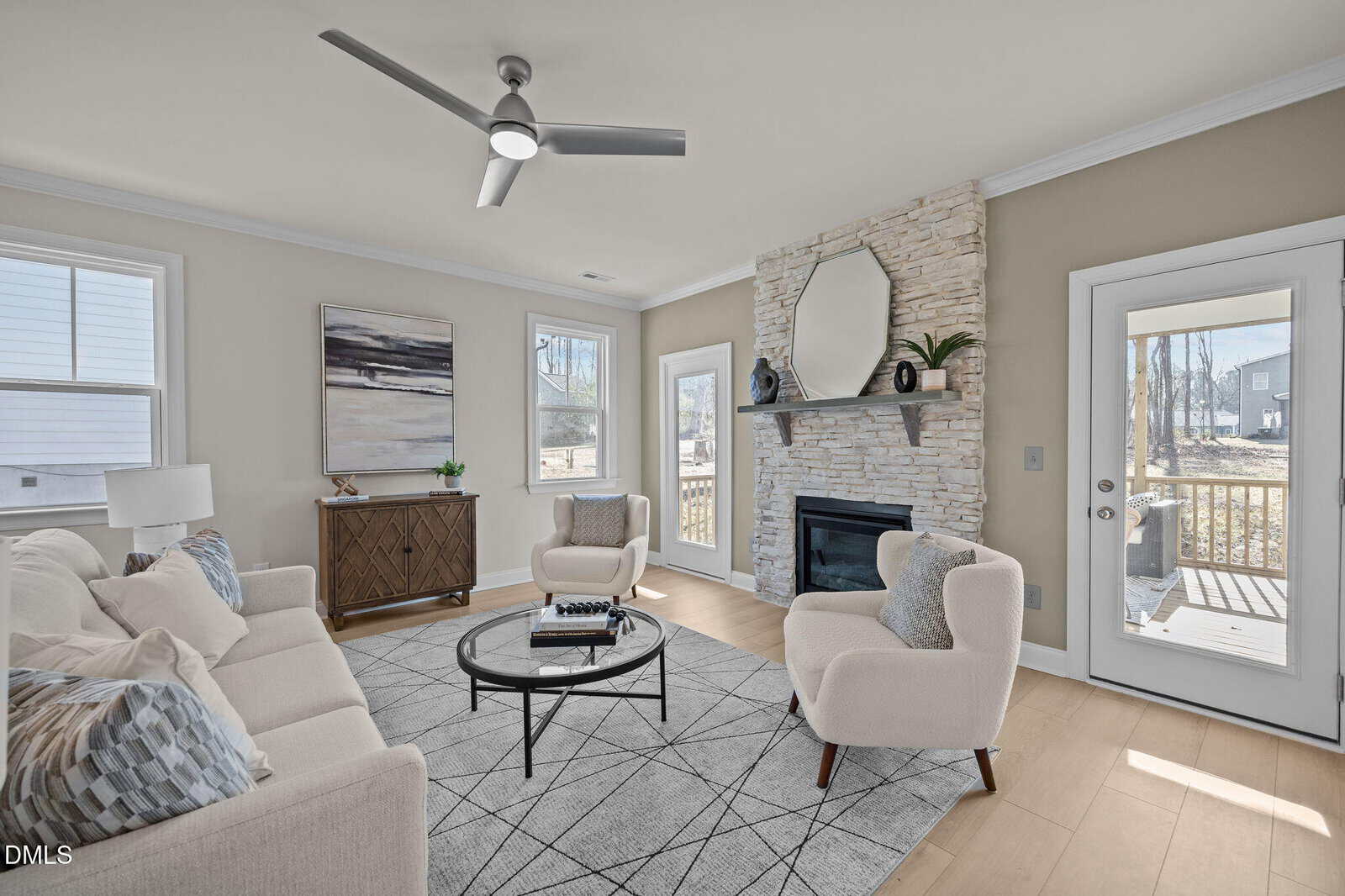 Modern living room with light-colored furniture, a round glass coffee table, stone fireplace, and large mirror above the mantel. Windows and a glass door let in natural light, and neutral tones create an inviting atmosphere.