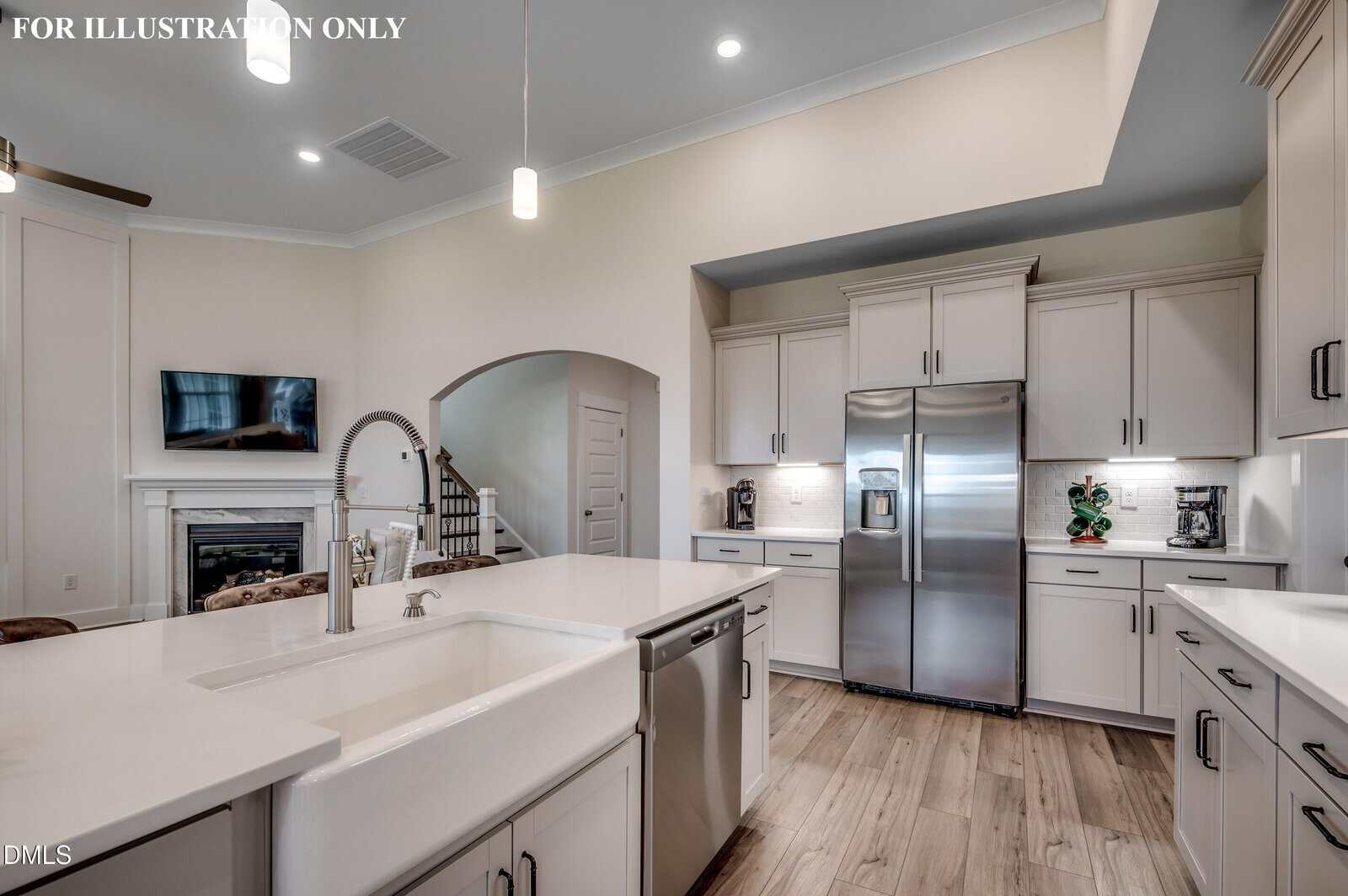 Modern kitchen with white cabinets, stainless steel appliances, a farmhouse sink, island with dishwasher, and wood flooring. An open archway leads to a staircase and living area with a fireplace and TV in the background.