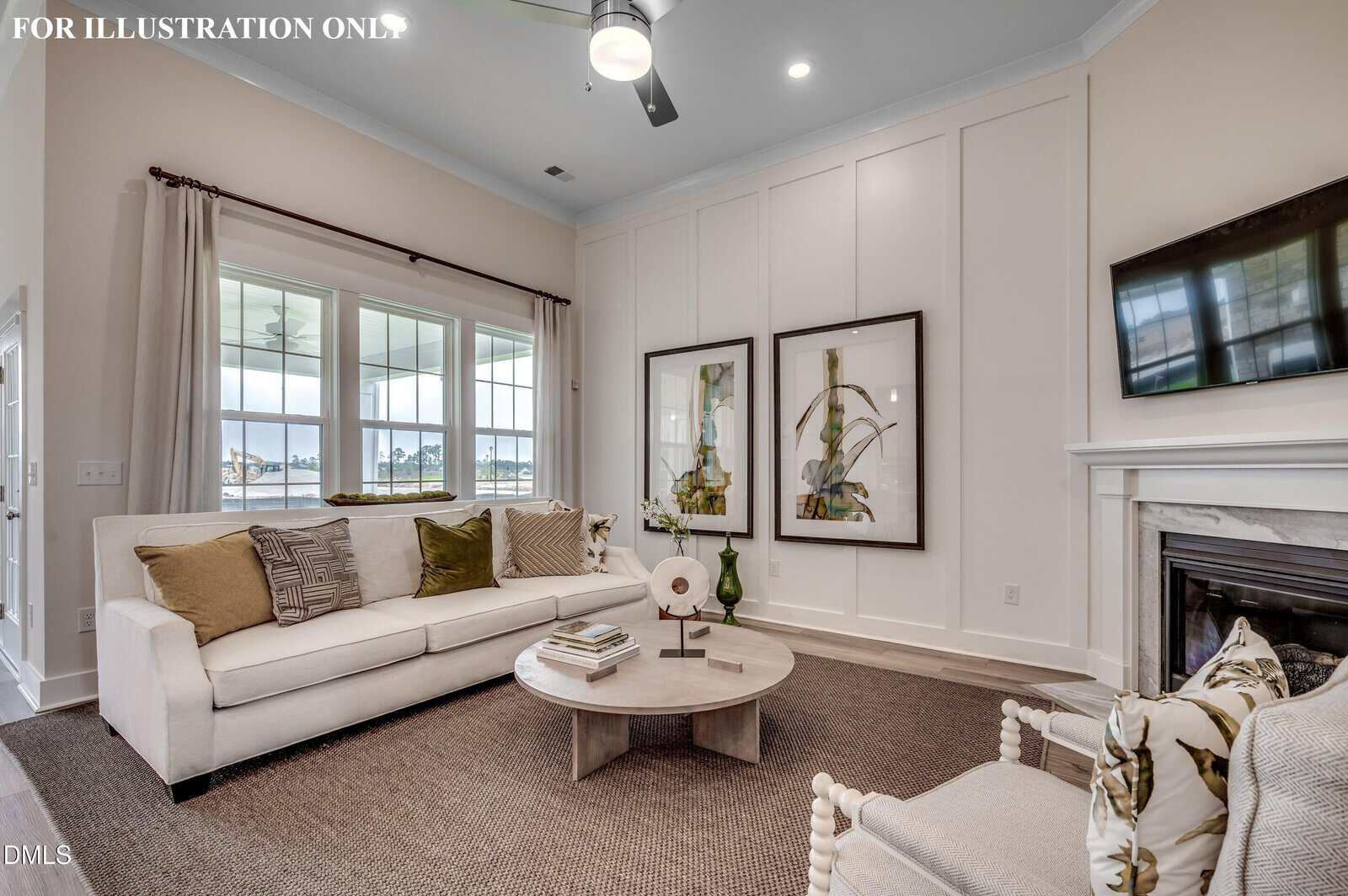 Bright living room with a white sofa, beige and brown cushions, armchair, round coffee table, fireplace with a TV above, two botanical art pieces, and large windows with light curtains, letting in natural light.