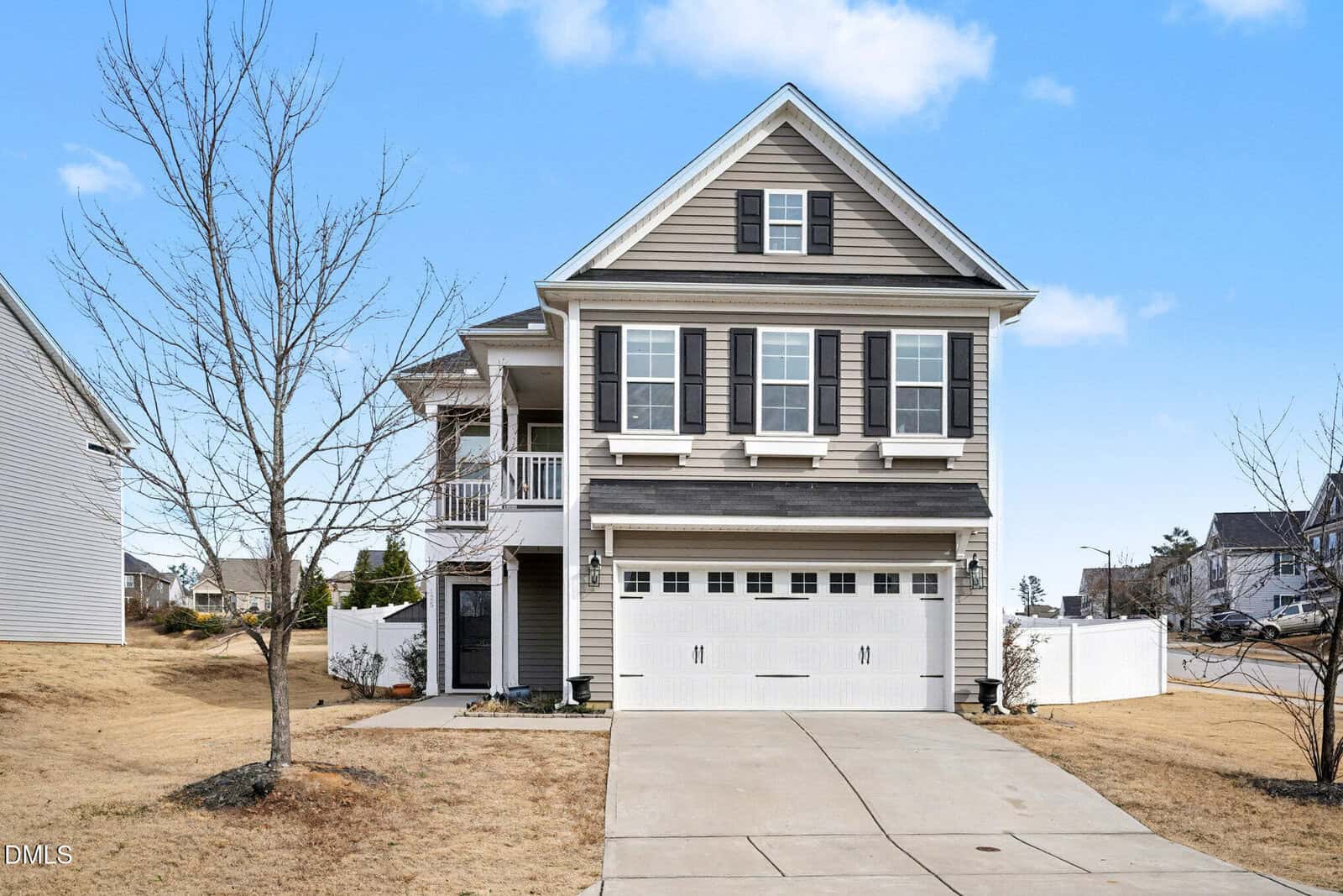 This two-story suburban home at 125 Flat Shoal Lane, Franklinton, features beige siding, dark shutters, and a double garage. A driveway leads to the garage, with a leafless tree in the front yard beneath a mostly clear sky.