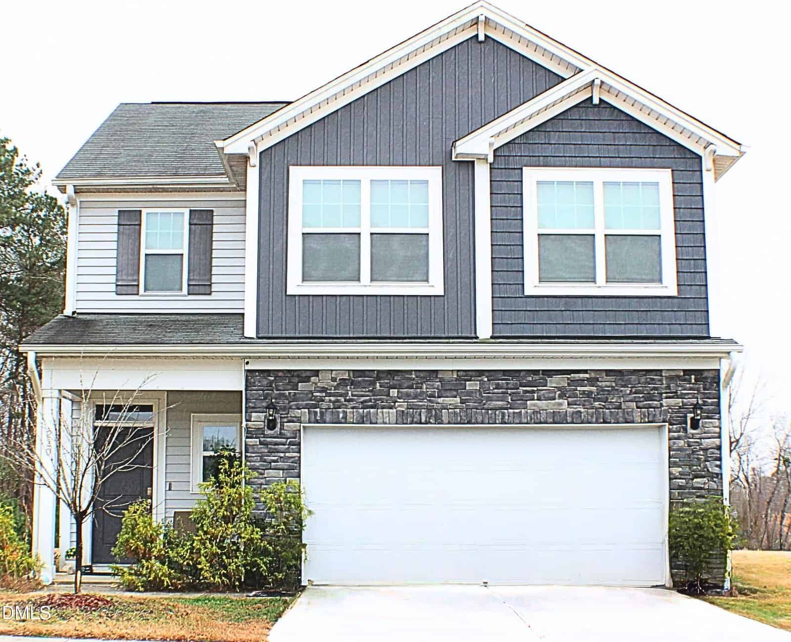 A two-story suburban house at 220 Hawksbill Drive, Franklinton, with gray siding, a double garage, stone accents on the lower front, and white-framed windows. Small shrubs line the front, and a bare tree is on the left.