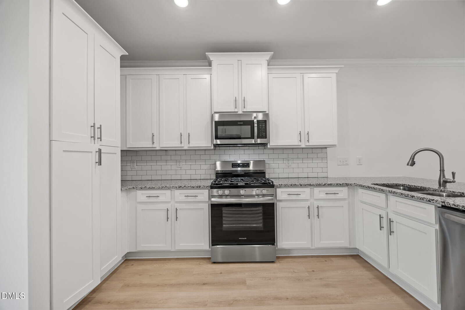 Modern kitchen with white cabinets, stainless steel appliances including a gas stove and microwave, granite countertops, subway tile backsplash, light wood flooring, and a sink with a high-arc faucet.